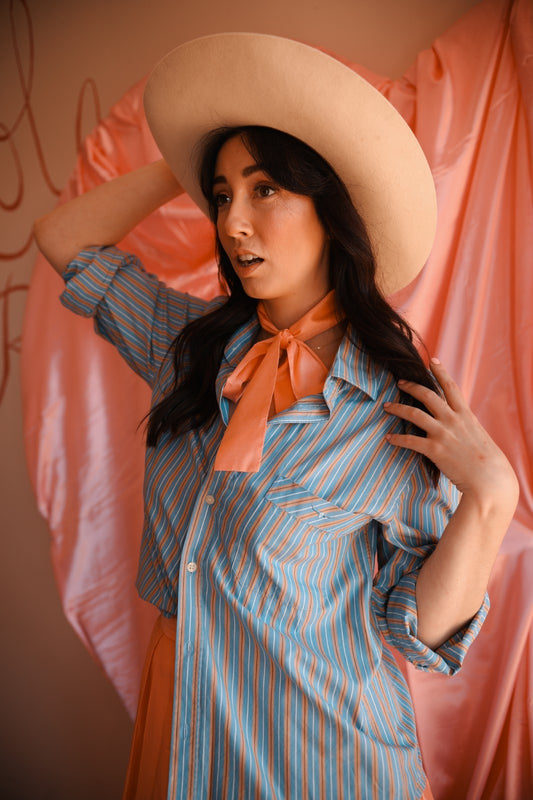 Woman wearing a striped shirt and wide-brimmed hat against a pink curtain.