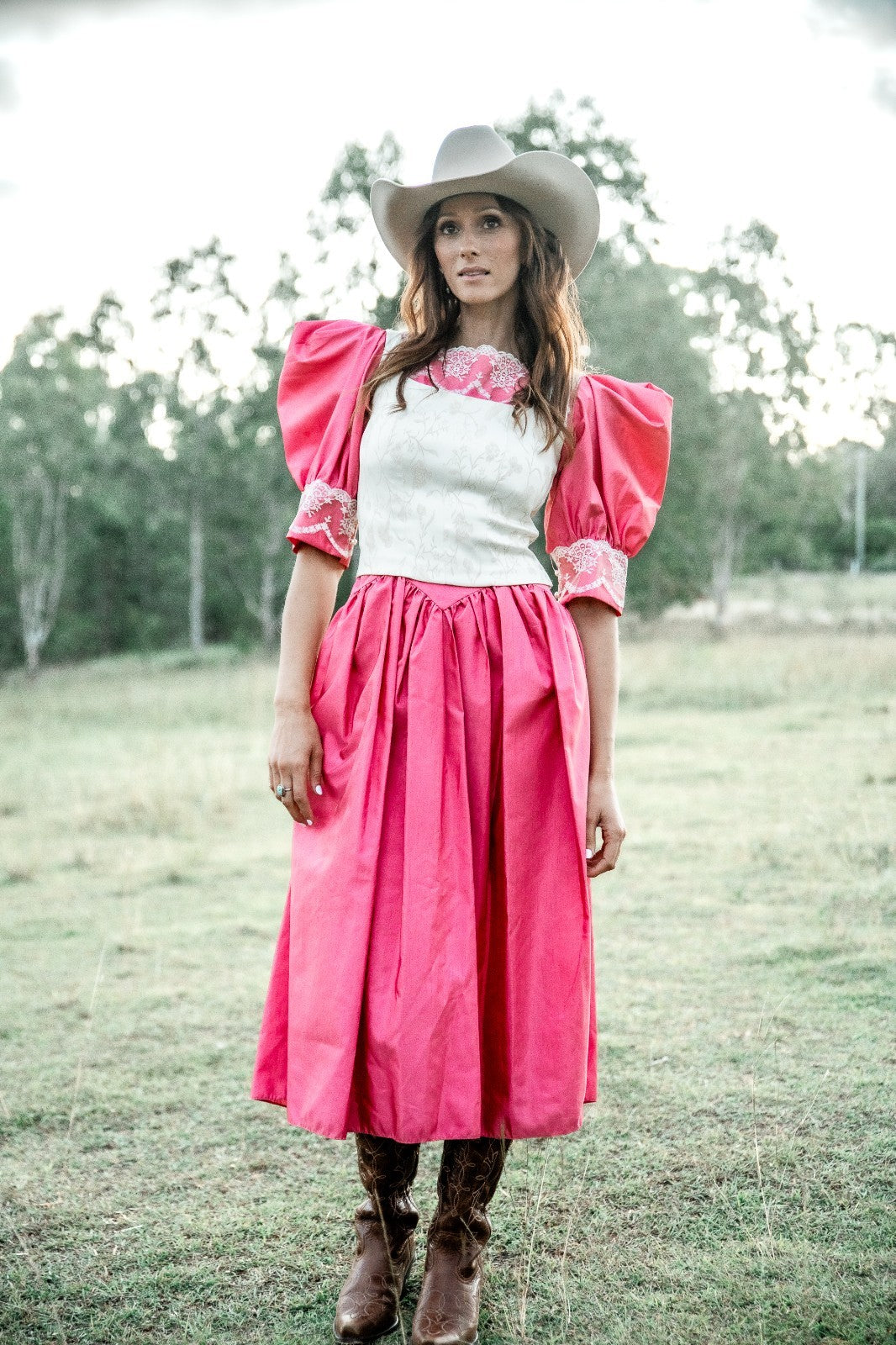 Woman in a pink dress with puffed sleeves and white top, standing in a grassy field.