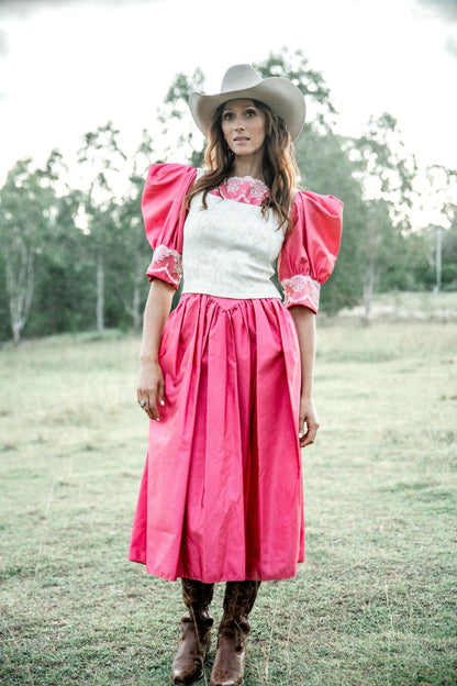 Woman in a pink dress with puffed sleeves and white top, standing in a grassy field.