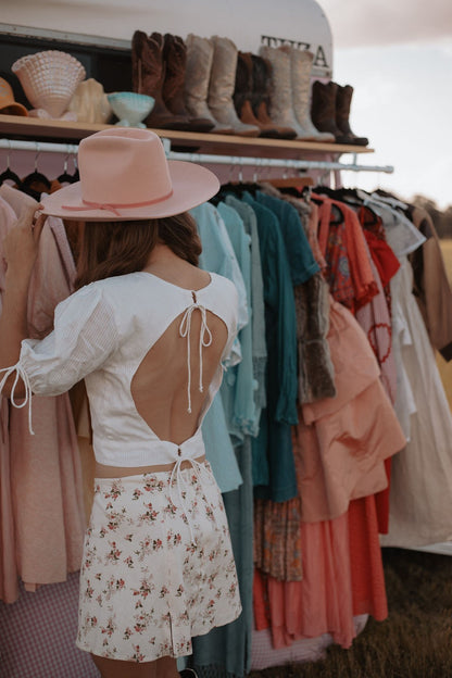 Person wearing a pink hat and white dress with cut-out back in a clothing store.