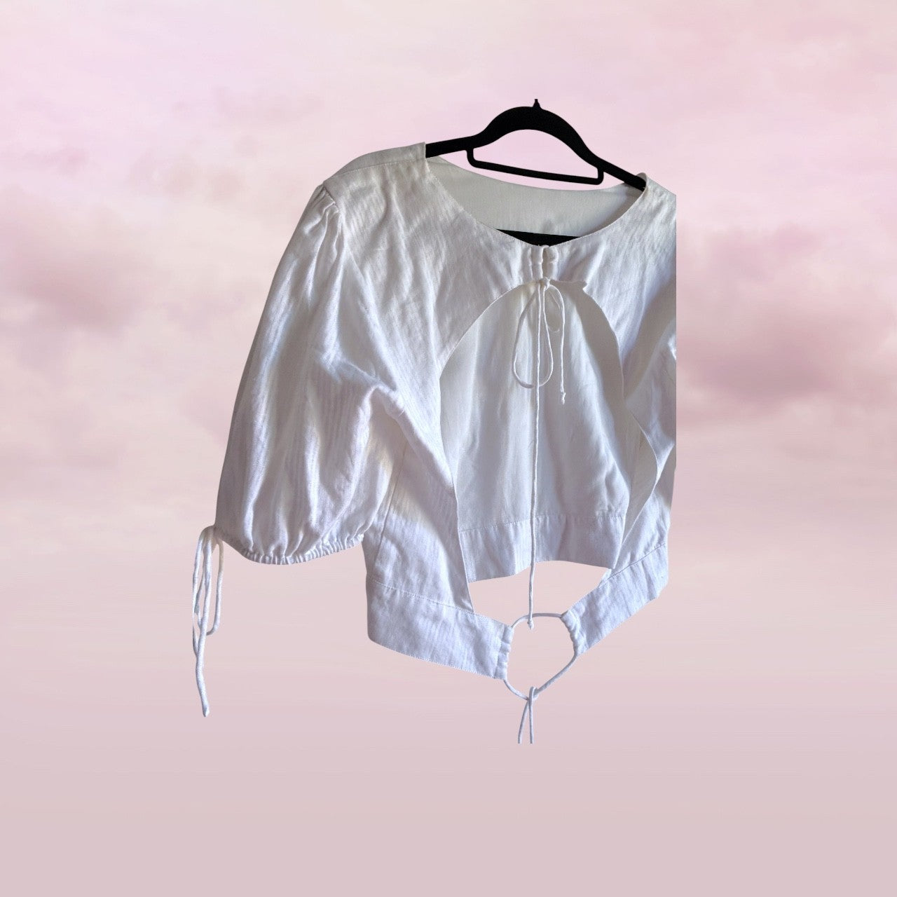 White blouse with short sleeves on a hanger against a pink background