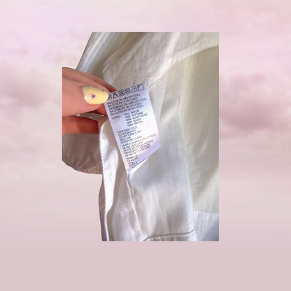 Close-up of a silver jacket with a label held by a hand against a pink background