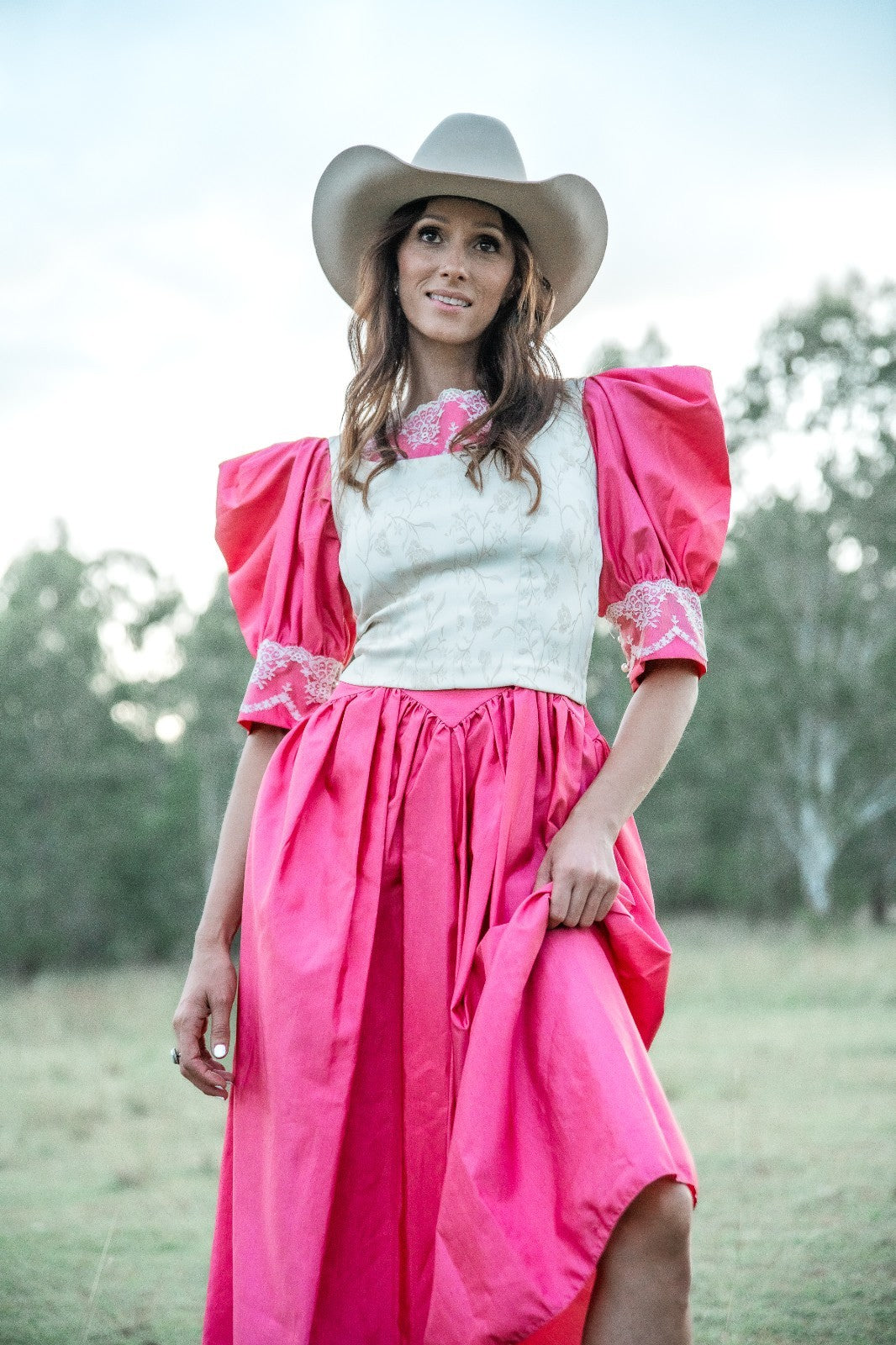 Woman wearing a pink dress and white cowboy hat in an outdoor setting