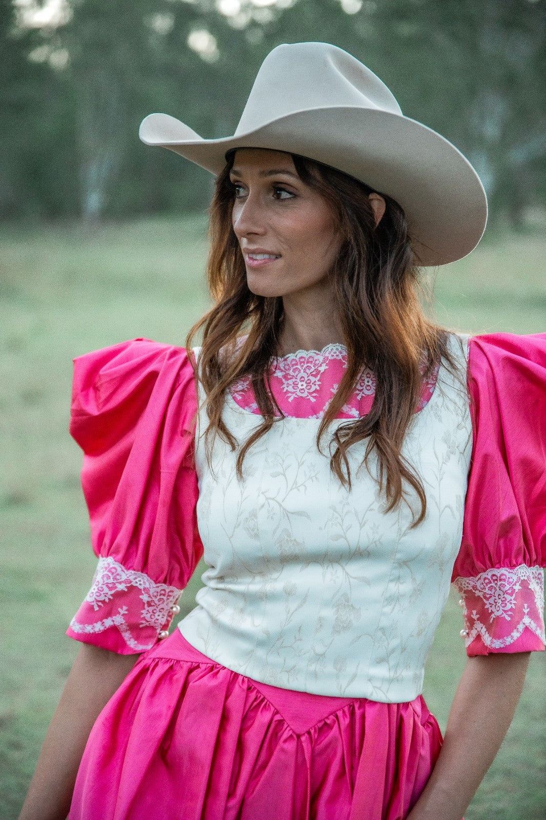 Woman wearing a pink and white outfit with a cowboy hat in an outdoor setting