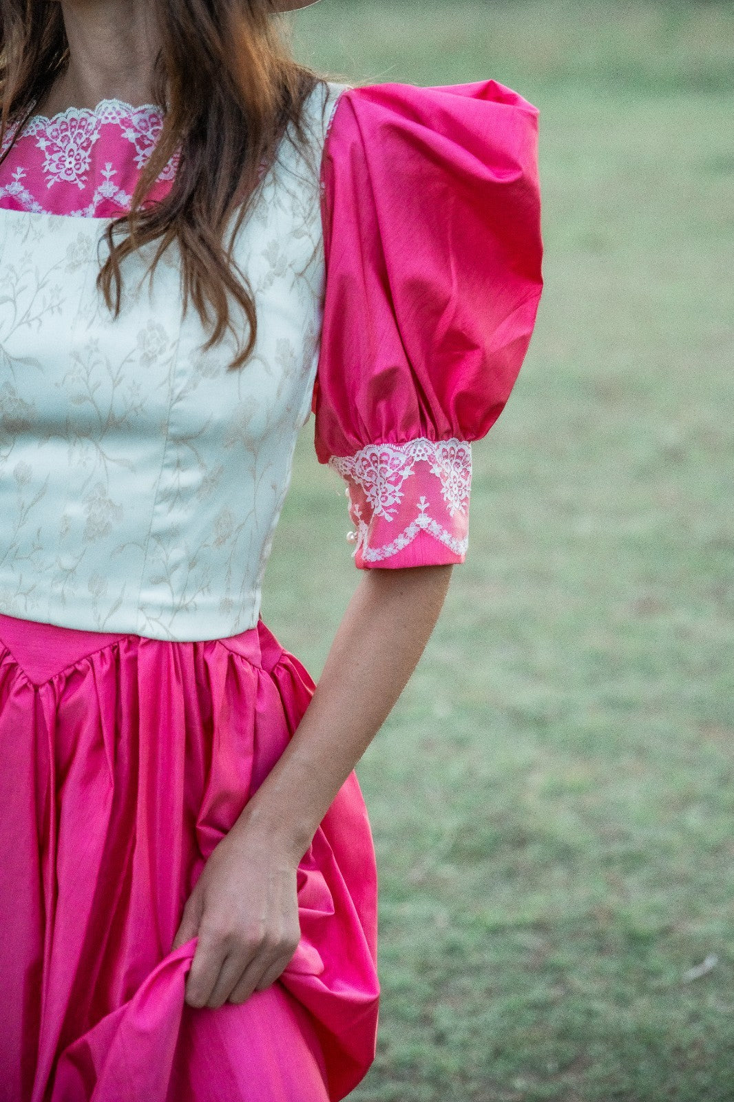 Person wearing a white top with pink sleeves and skirt against a blurred green background