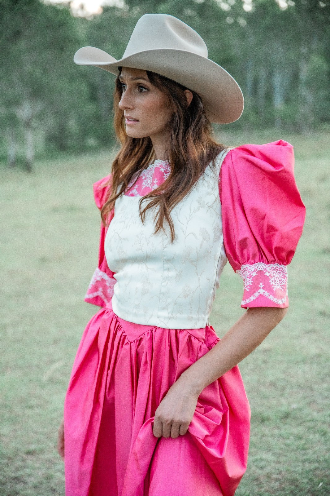 Woman wearing a pink dress with white lace top and cowboy hat in a natural setting