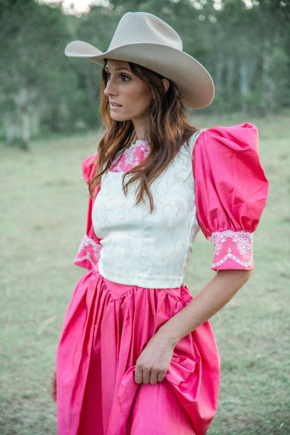 Woman wearing a pink dress with white lace top and cowboy hat in a natural setting
