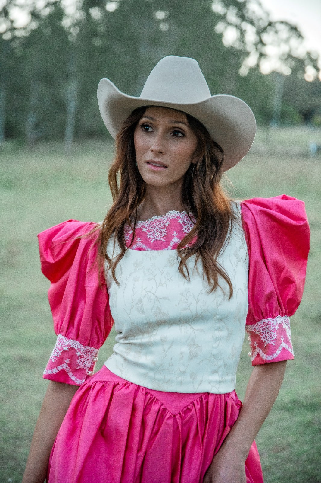 Woman wearing a pink and white outfit with a cowboy hat in an outdoor setting