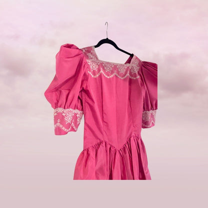 Pink dress with lace details on a hanger against a light pink background