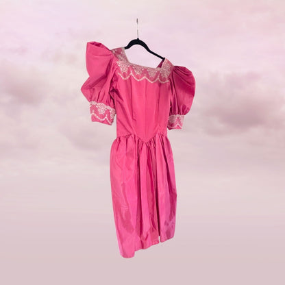 Pink dress with lace details on a hanger against a pink background