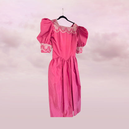 Pink dress with lace details on a hanger against a pink background