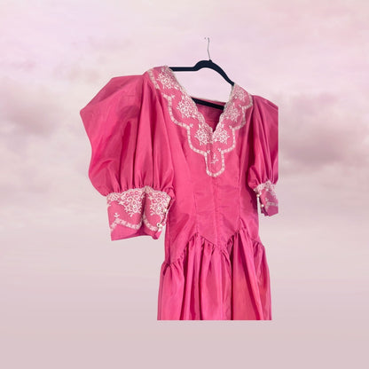 Pink dress with white lace details on a hanger against a pink background