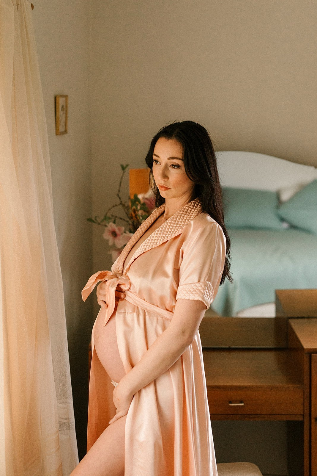 Woman in a peach satin robe standing in a bedroom.