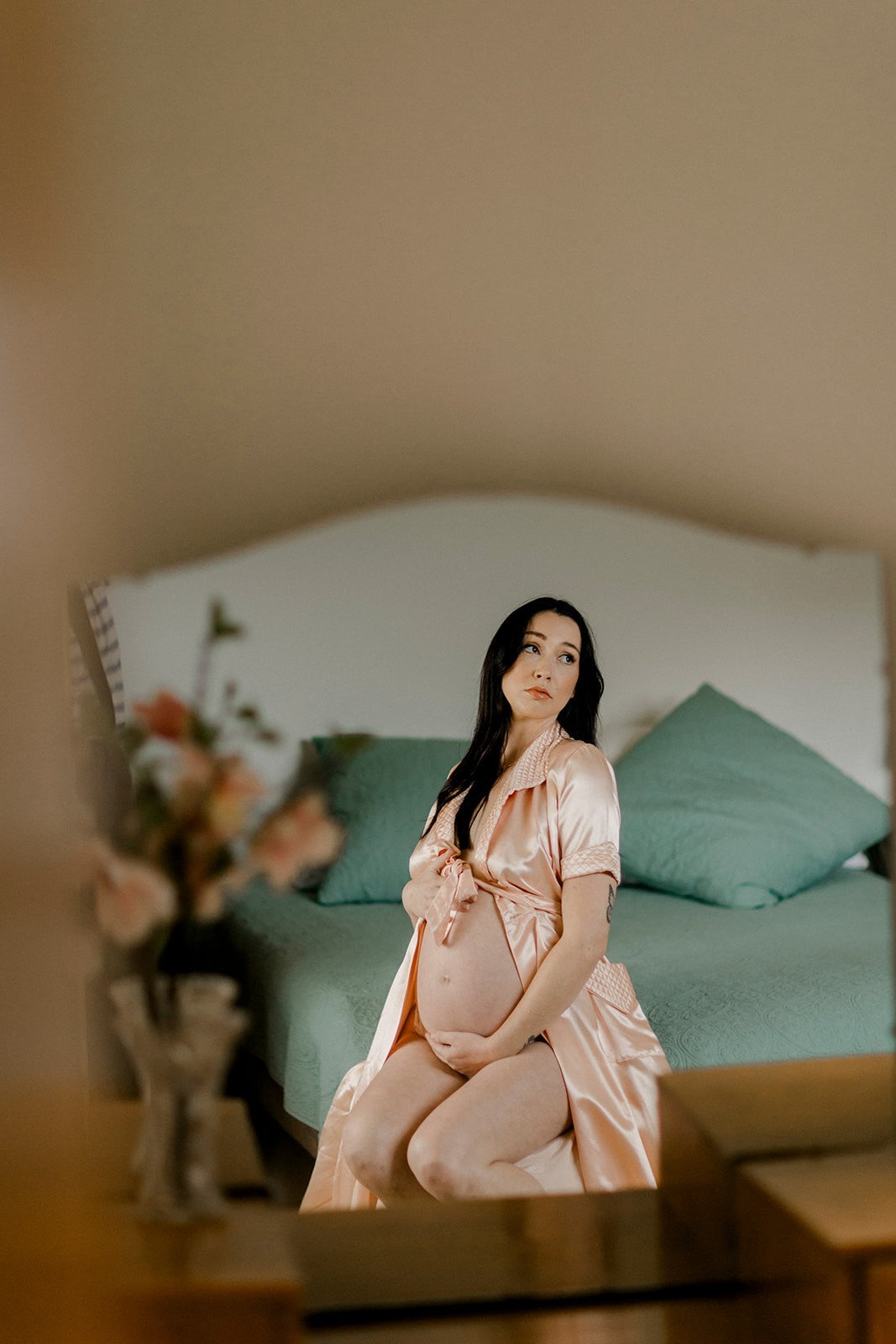 Pregnant woman in a pink dress sitting on a bed with a blurred background