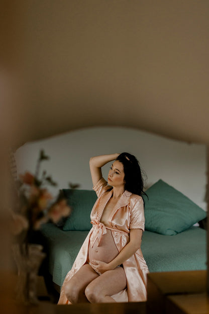 Woman in a pink robe sitting on a bed with teal pillows, surrounded by flowers.