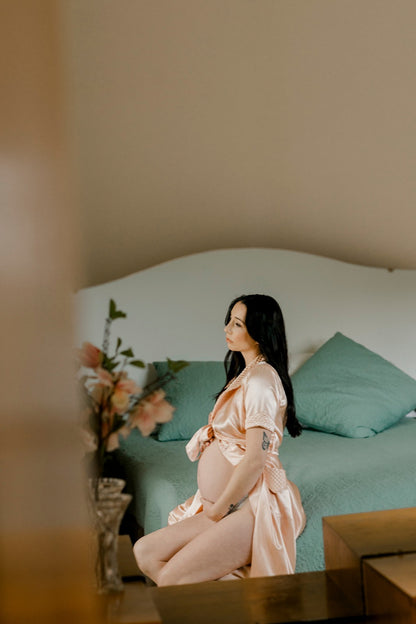 Pregnant woman in a pink robe sitting on a bed with a blurred background