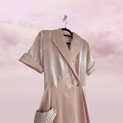 Pink satin robe with quilted details on a hanger against a pink background