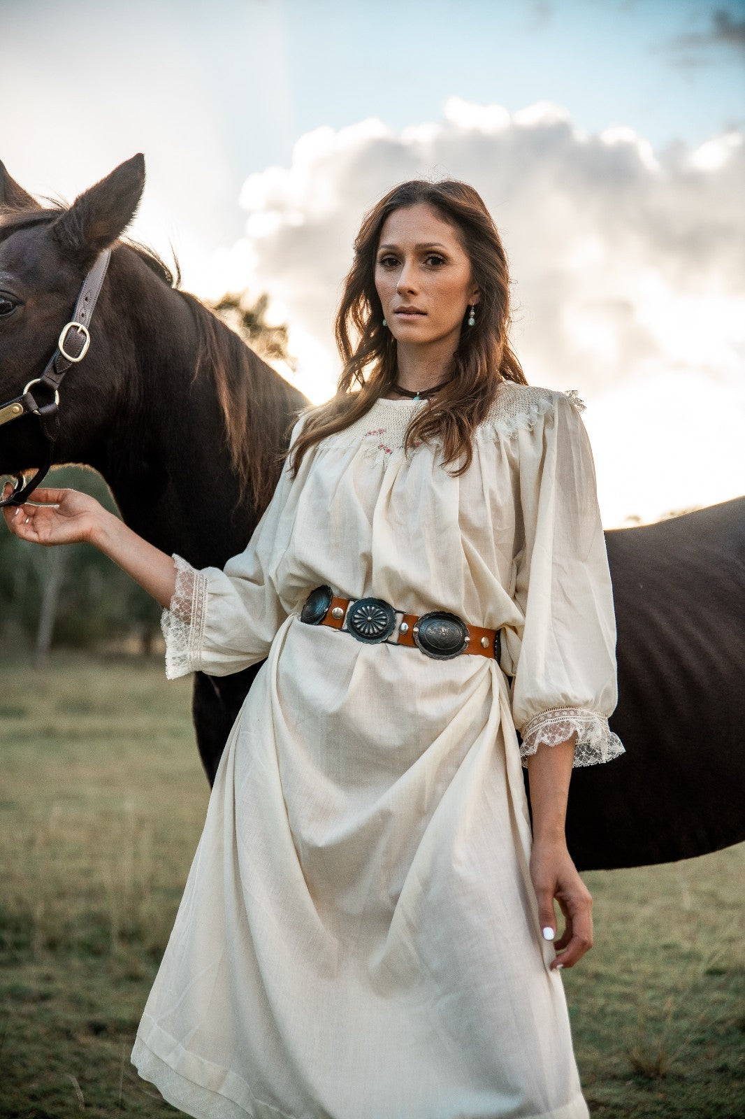 Woman in a white dress standing next to a horse in an outdoor setting