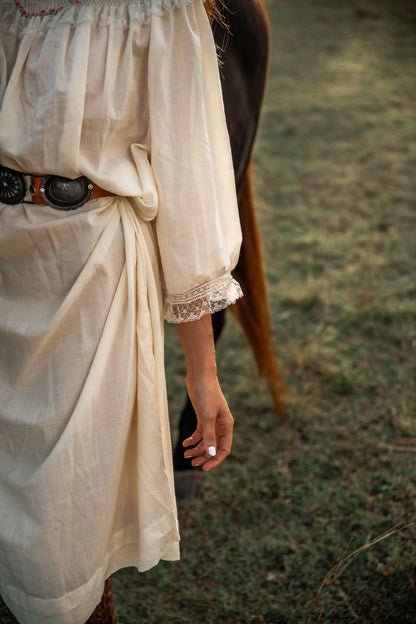 Person wearing a beige dress with a belt in a natural setting