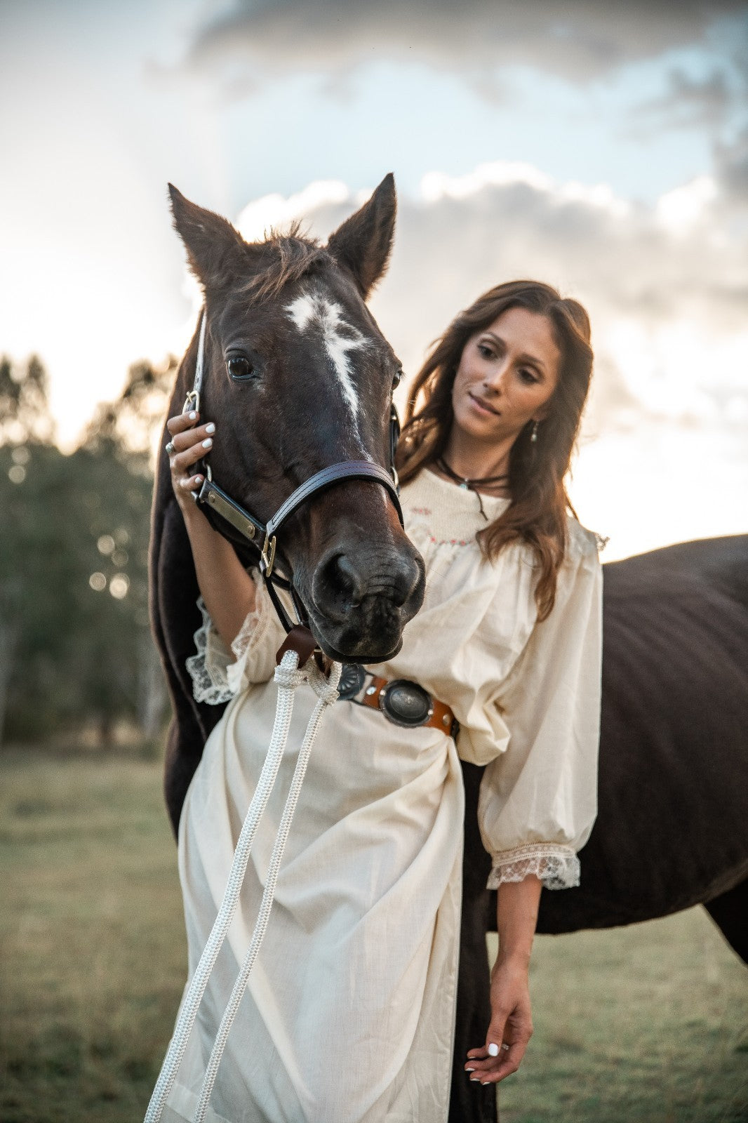 Woman in a white dress standing next to a horse in an outdoor setting
