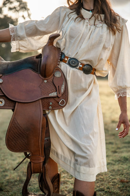 Person holding a brown leather saddle in a natural setting