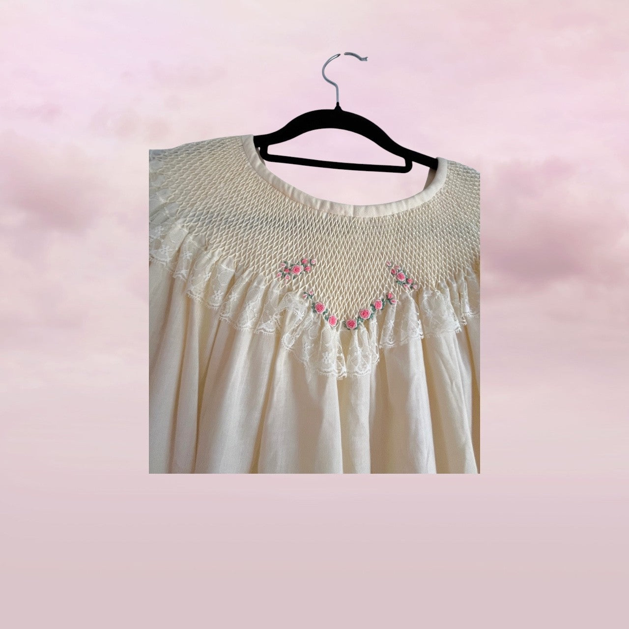 White lace dress with pink floral embroidery on a hanger against a pink background