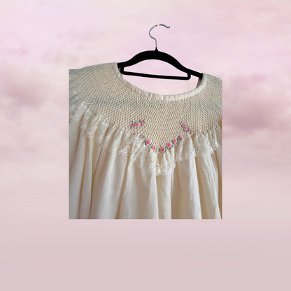 White lace dress with pink floral embroidery on a hanger against a pink background
