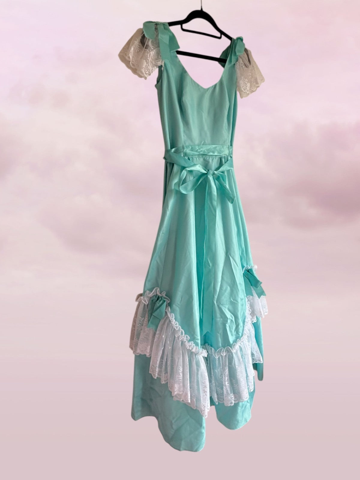 Teal dress with lace details on a hanger against a pink background