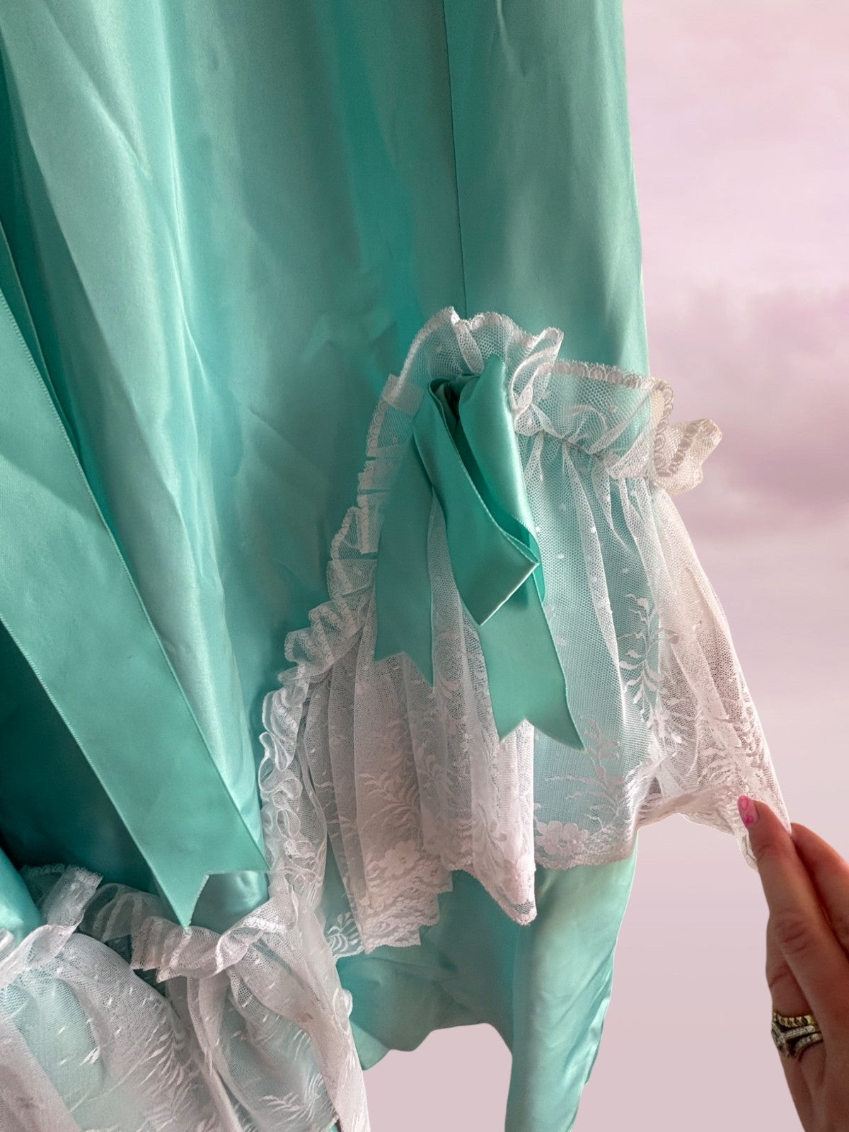 Close-up of a turquoise dress with lace details on a pink background