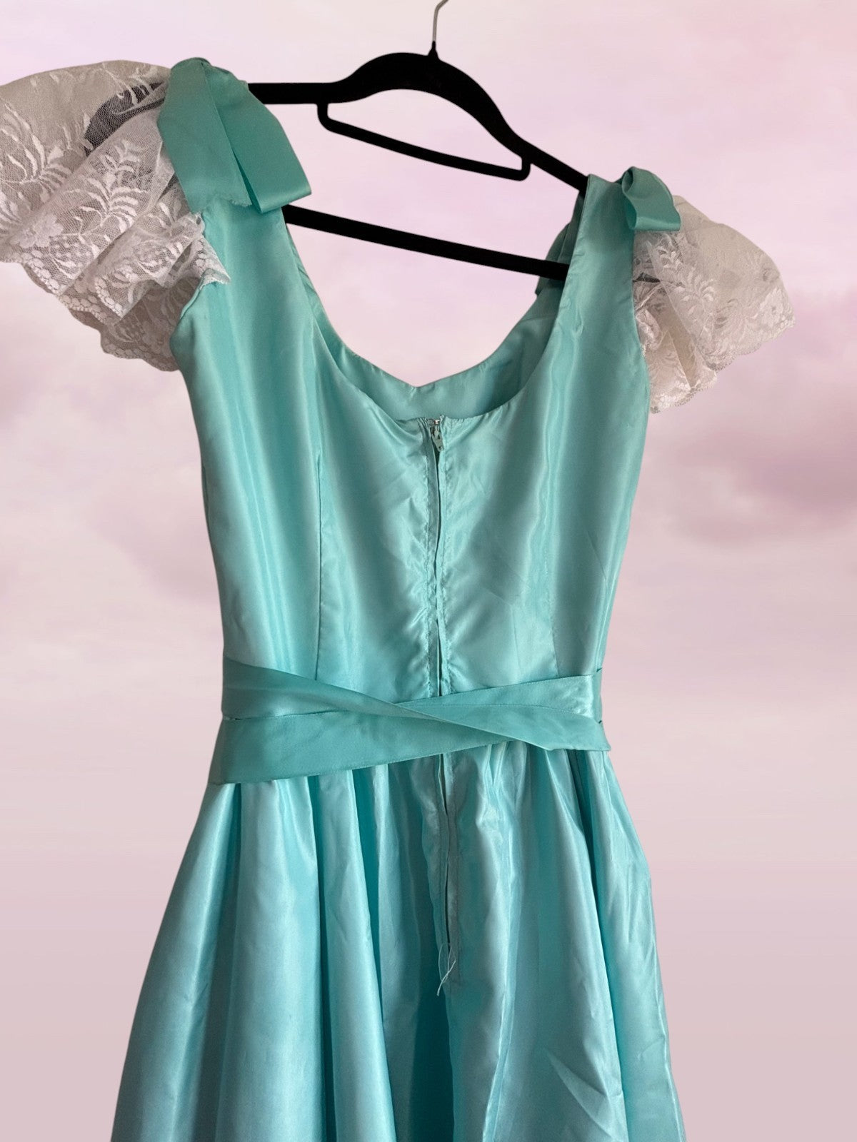Teal dress on a hanger against a light pink background