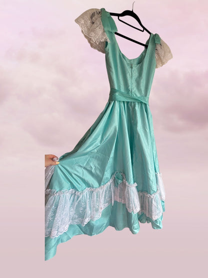 Teal dress with lace details on a hanger against a pink background