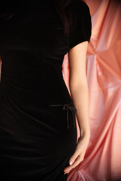 Person wearing a black dress with a soft pink fabric background