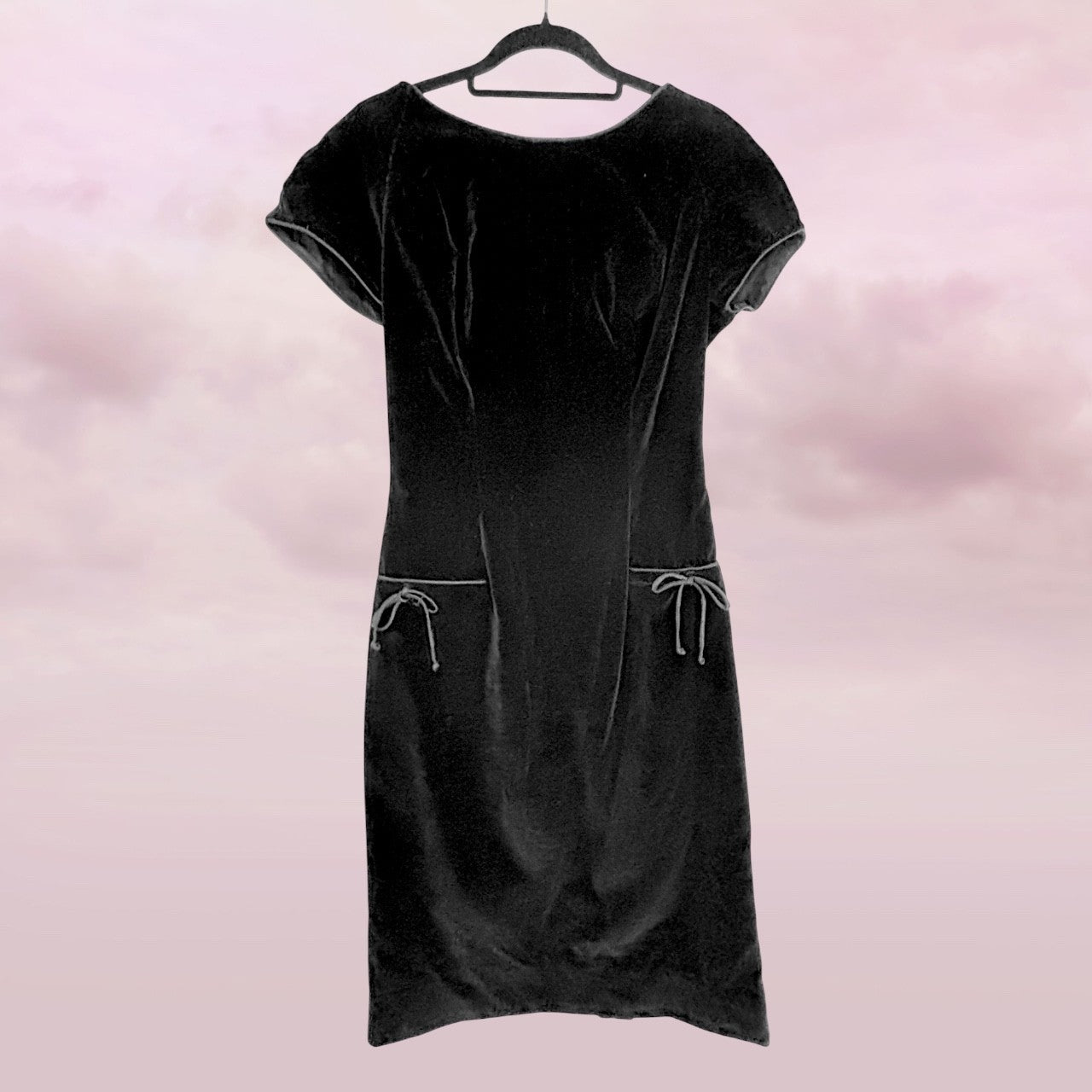 Black velvet dress on a hanger against a pink background