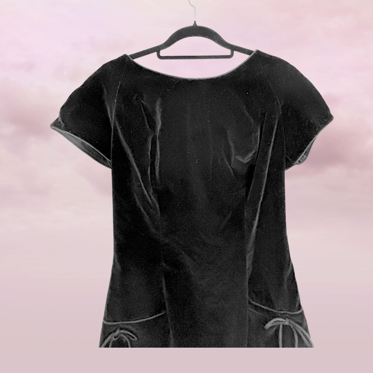 Black velvet dress on a hanger against a pink background