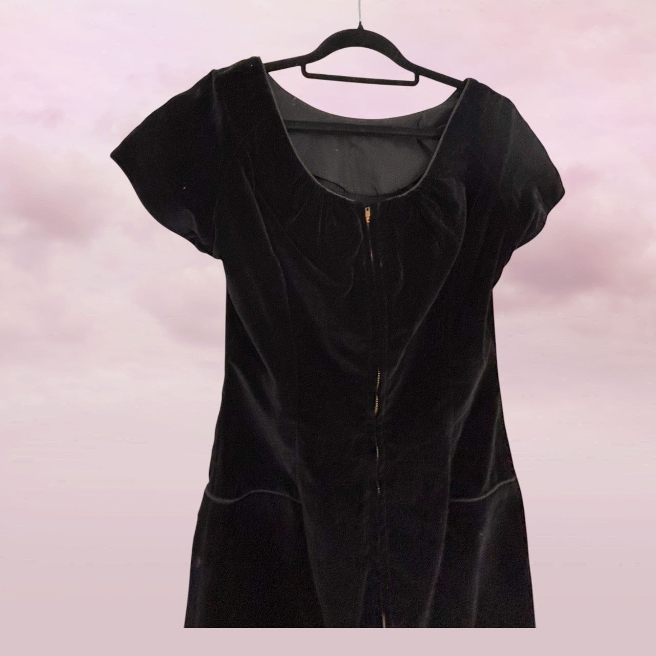 Black velvet dress on a hanger against a pink background