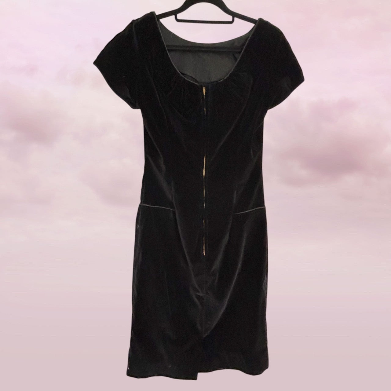 Black velvet dress on a hanger against a pink background