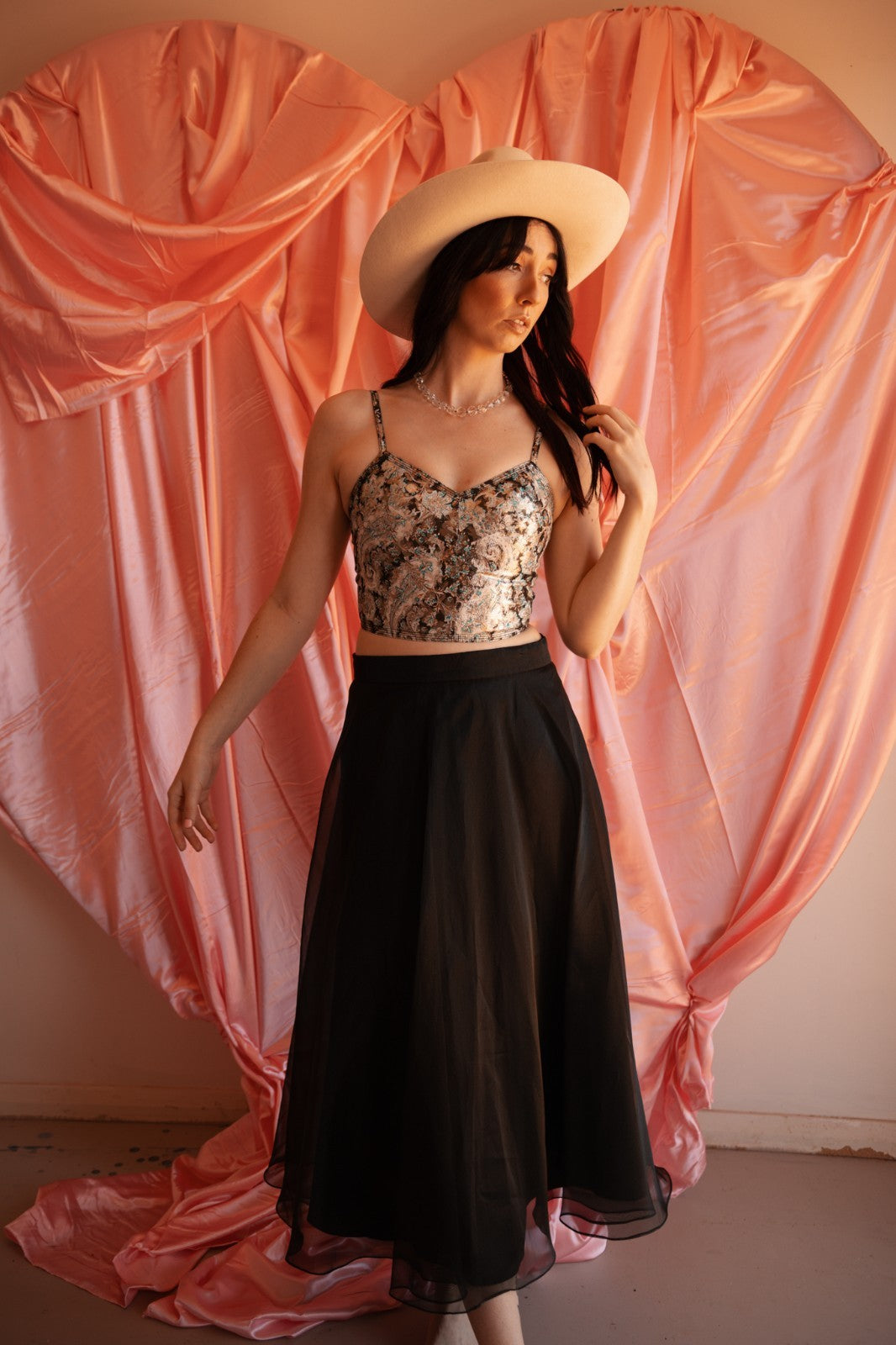 Woman wearing a floral top and black skirt against a pink draped curtain background