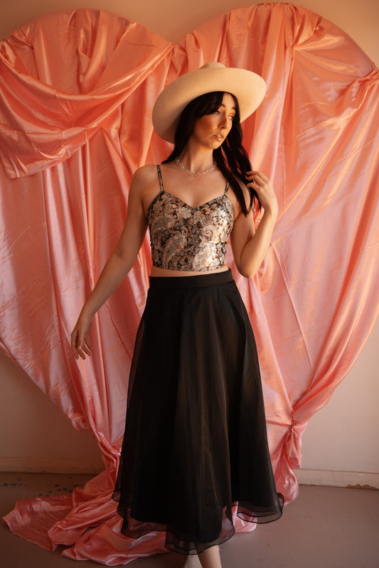 Woman wearing a floral top and black skirt against a pink draped curtain background