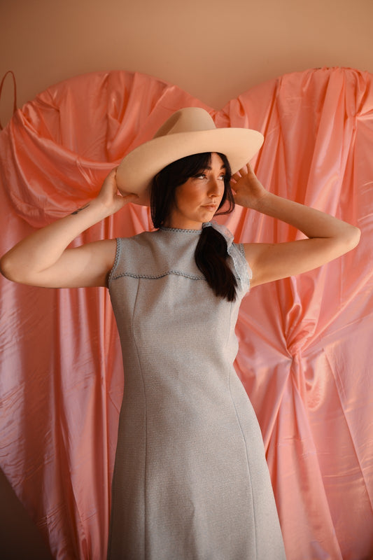 Woman wearing a light blue dress and beige hat against a pink curtain backdrop