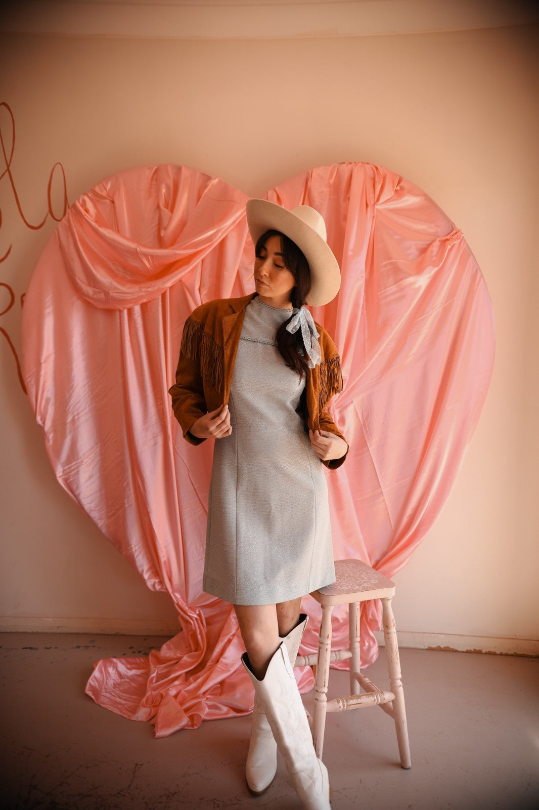 Woman in a dress and hat standing next to a pink heart-shaped curtain