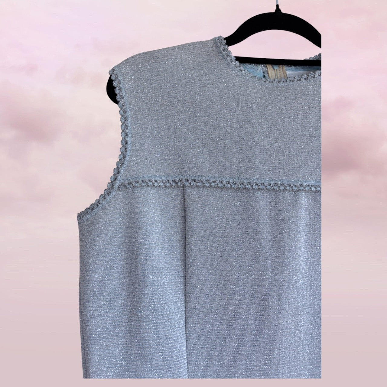 Light blue sleeveless top on a hanger against a pink background