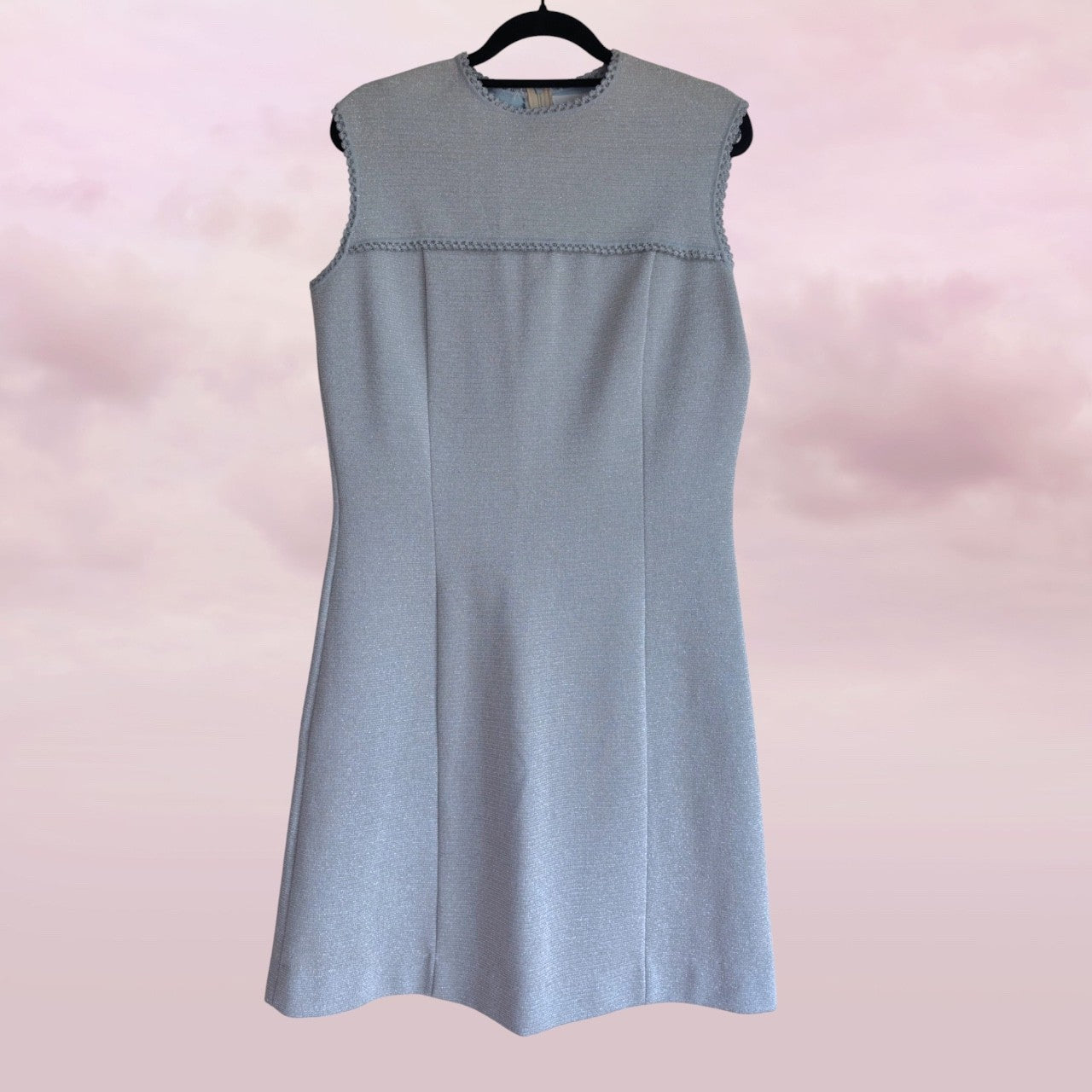 Light blue sleeveless dress on a hanger against a pink background
