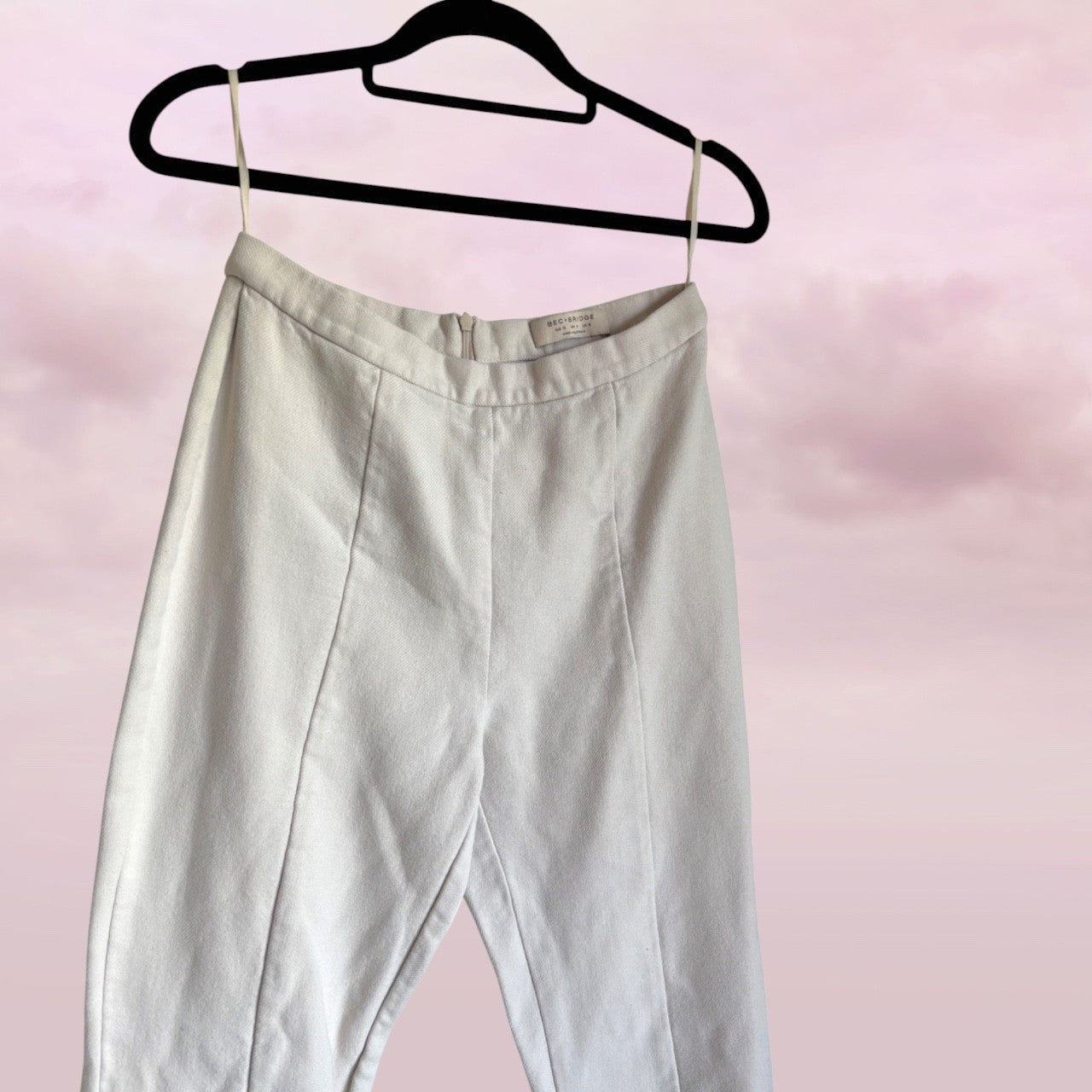 white pants on a black hanger against a pink background