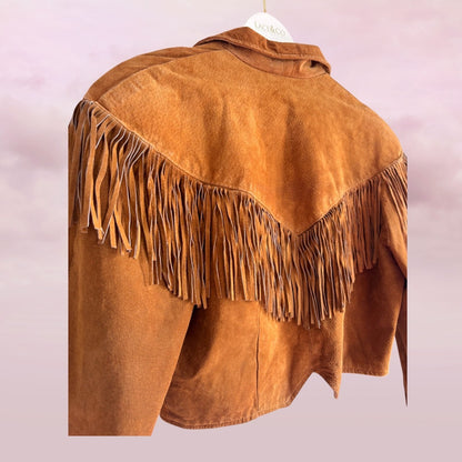 Brown suede jacket with fringes on a hanger against a light pink background
