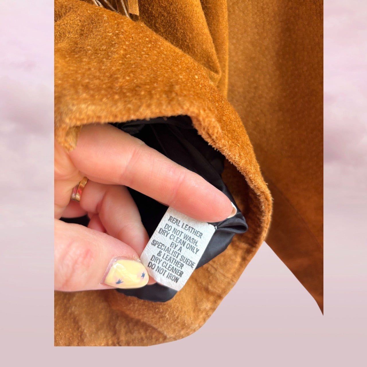 Hand holding a leather jacket label with text on a pink background