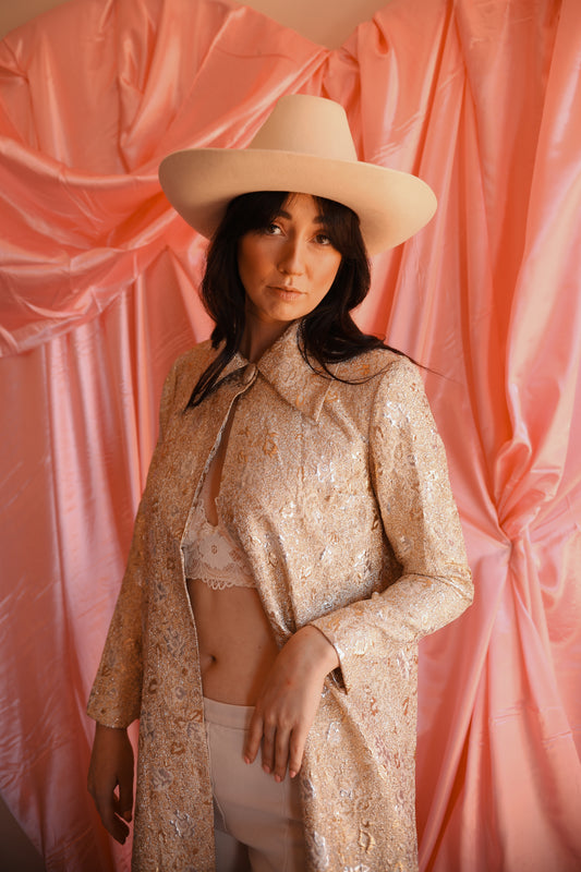 Woman wearing a beige hat and a patterned outfit against a pink curtain background