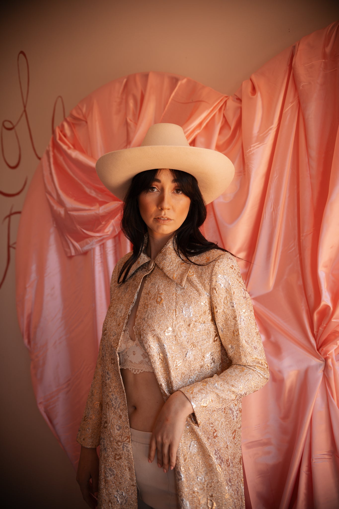 Woman wearing a beige hat and outfit against a pink draped fabric background