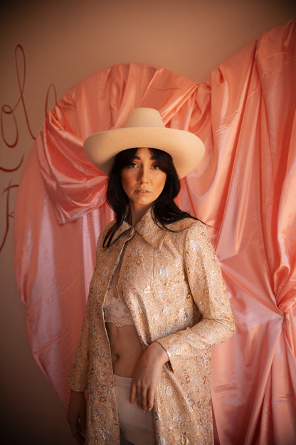 Woman wearing a beige hat and outfit against a pink draped fabric background
