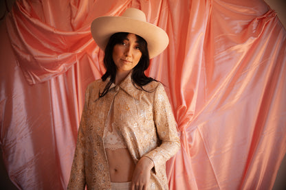 Woman wearing a beige hat and matching outfit against a pink draped fabric background