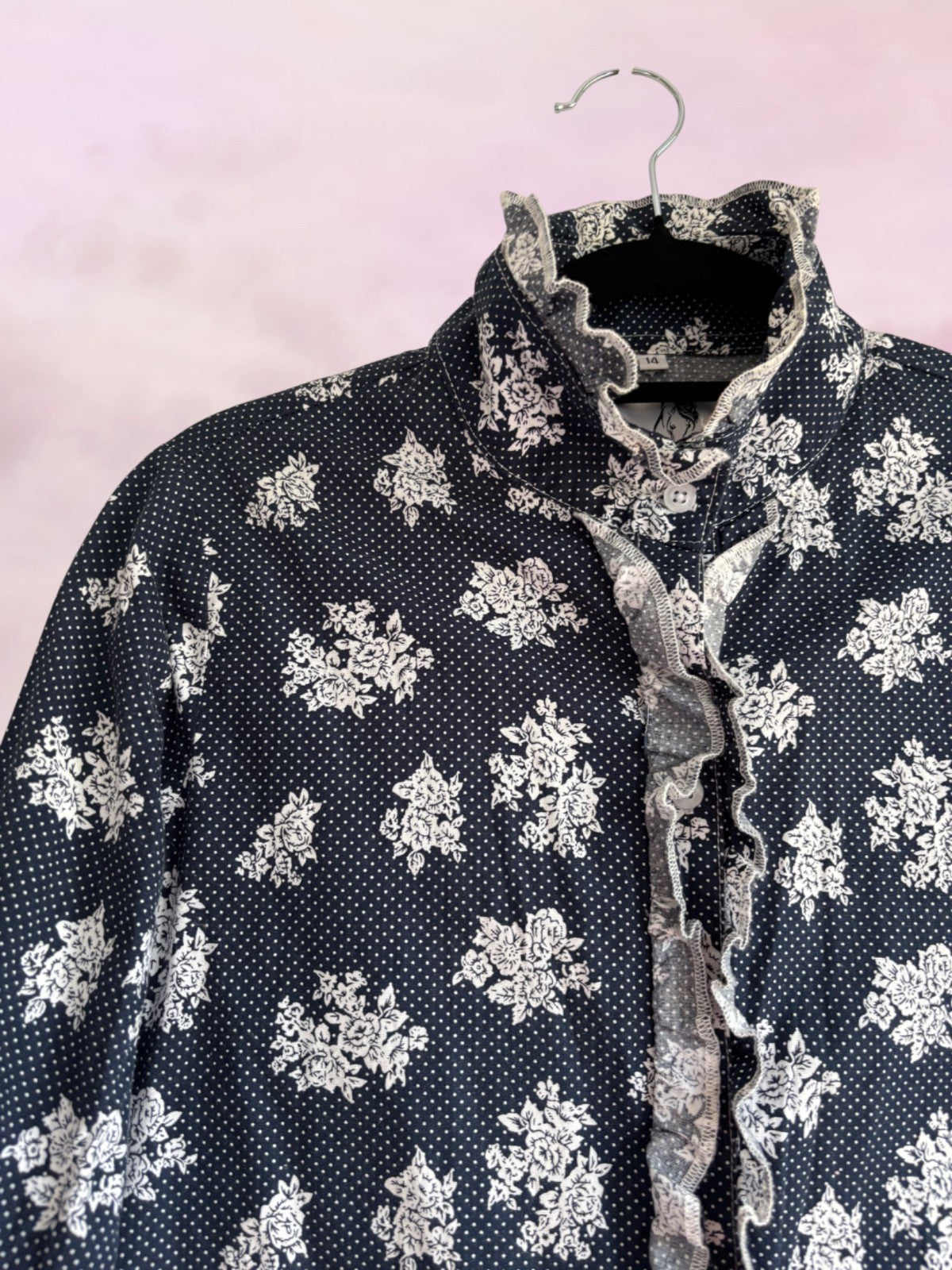 Black floral patterned shirt on a hanger against a pink background